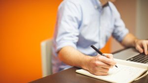 Personne rédigeant une note à la main à son bureau, avec un ordinateur portable ouvert, dans un bureau lumineux